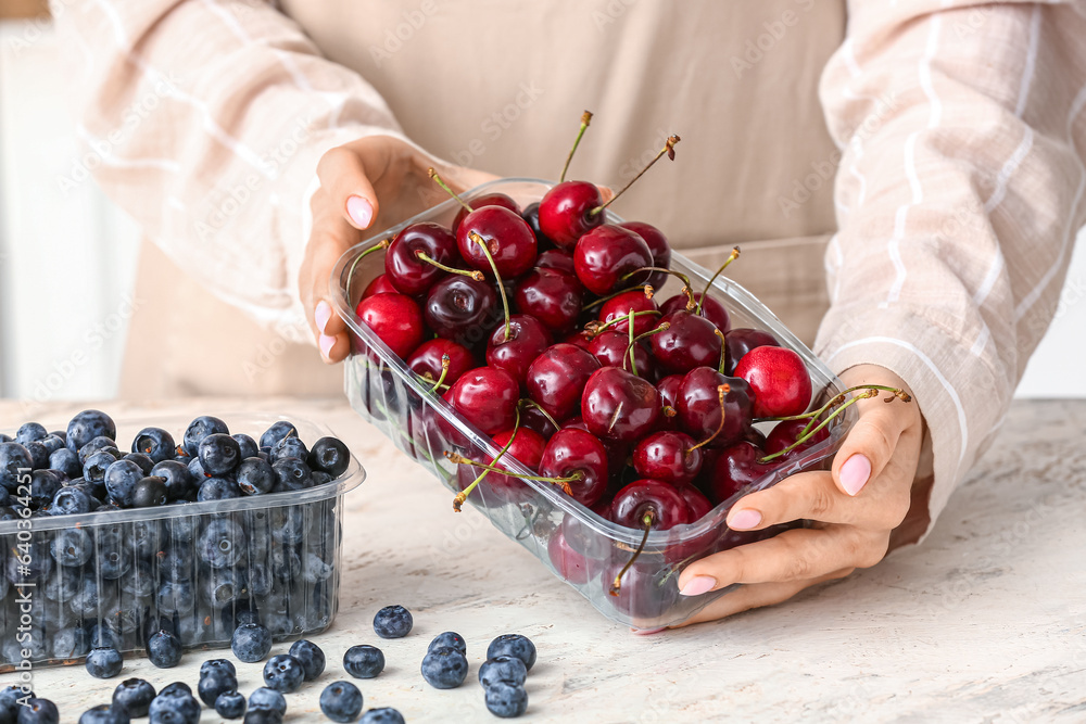 Woman holding plastic container with ripe cherries at table