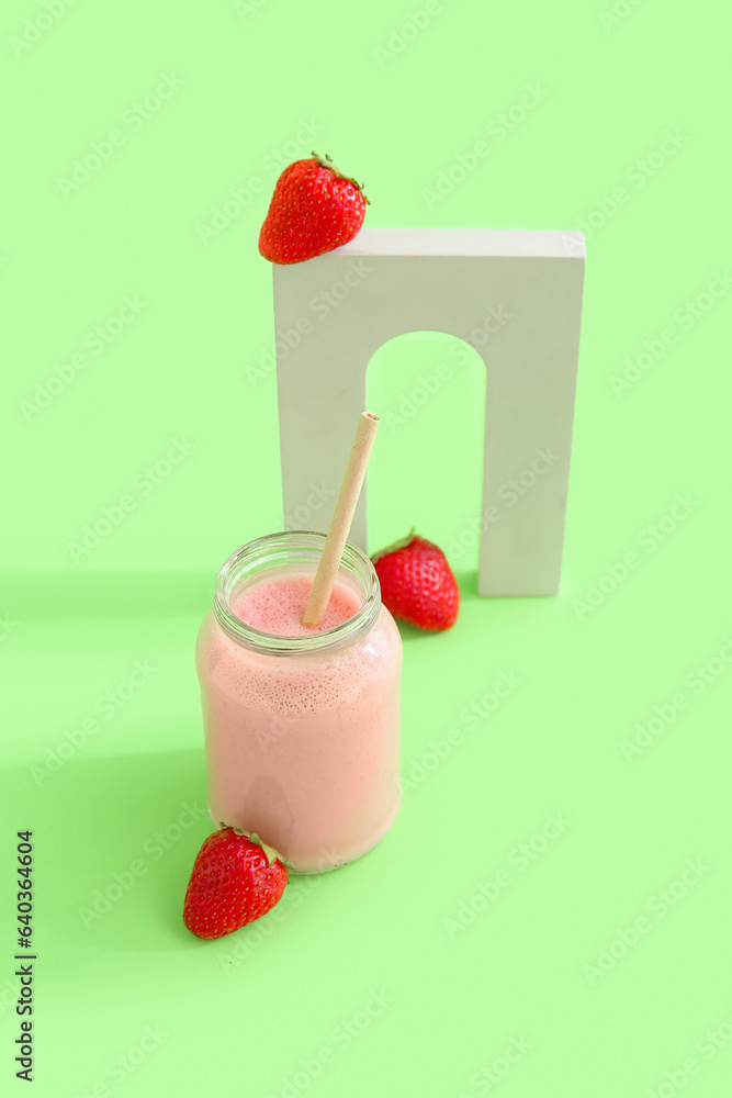 Mason jar of tasty strawberry smoothie on green background