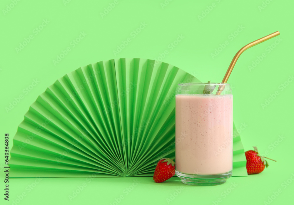 Glass of tasty strawberry smoothie with fan on green background