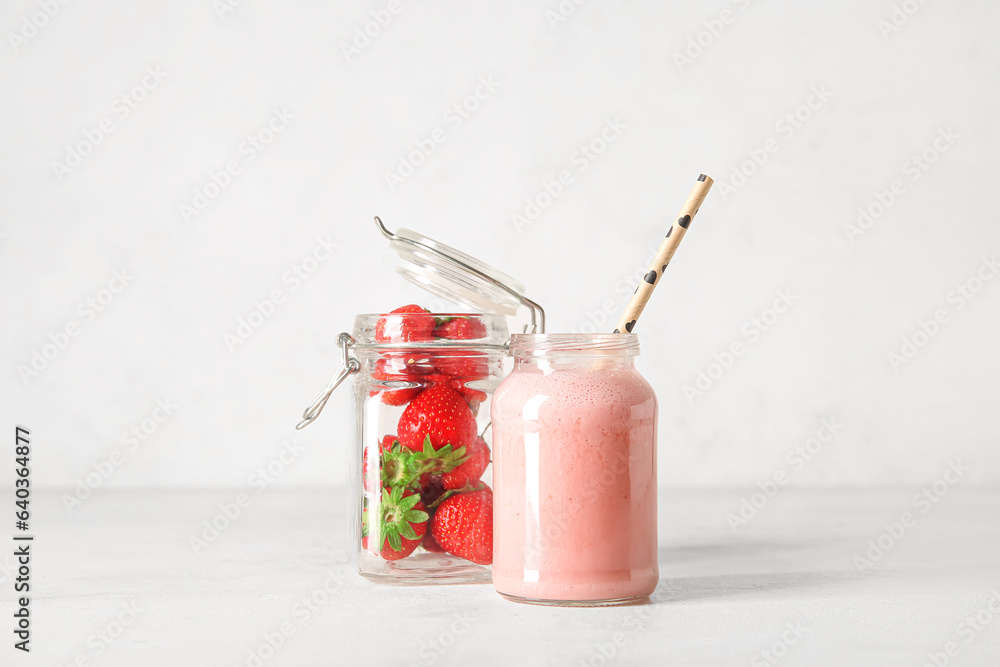 Mason jar of tasty strawberry smoothie on light background