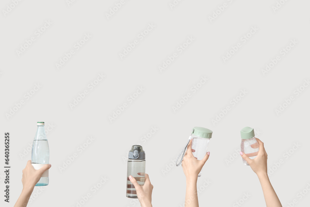 Female hands with bottles of fresh water on light background