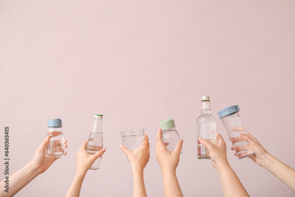 Female hands with bottles and glass of cold water on pink background