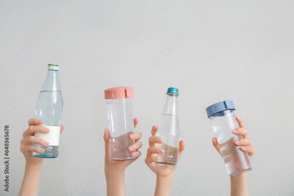 Female hands with bottles of cold water on light background