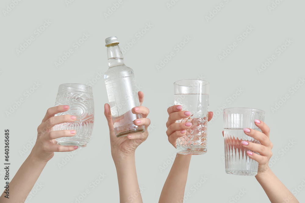 Female hands with bottle and glasses of cold water on light background