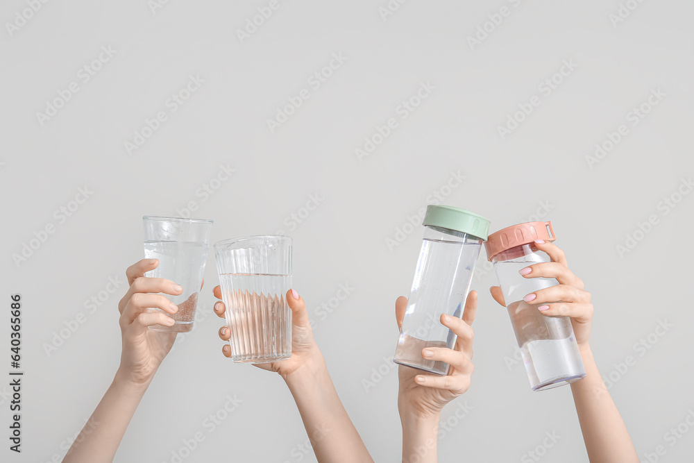 Female hands with bottles and glasses of cold water on light background