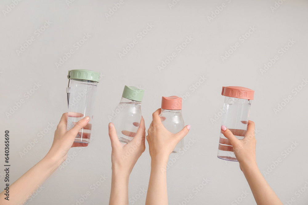 Female hands with bottles of cold water on light background