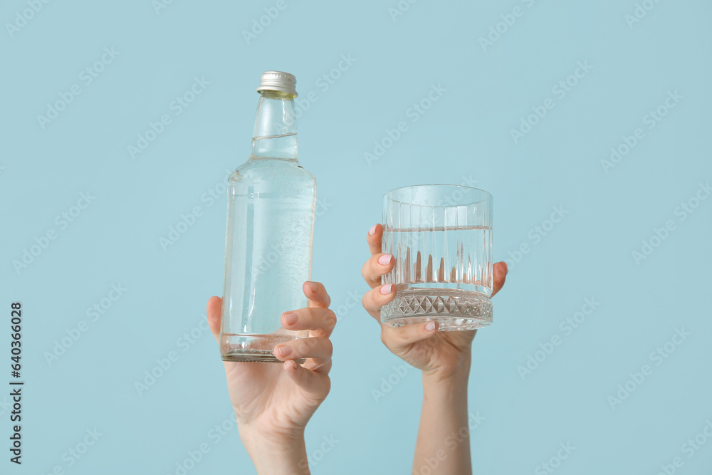 Female hands with bottle and glass of cold water on blue background