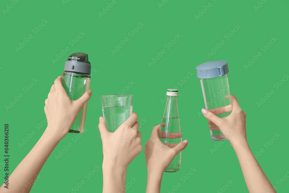 Female hands with bottles and glass of cold water on green background