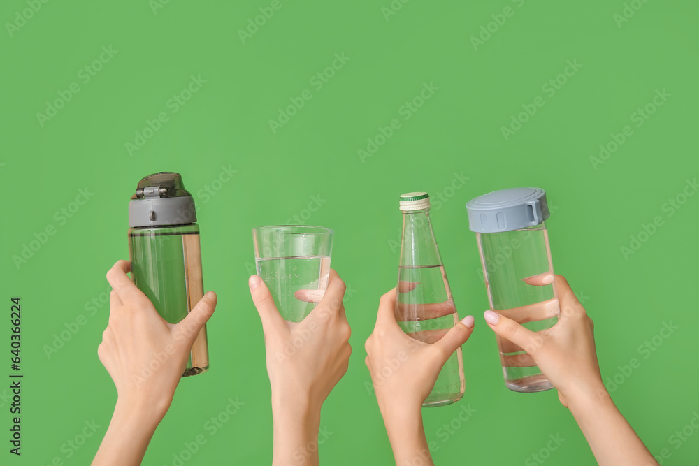 Female hands with bottles and glass of cold water on green background