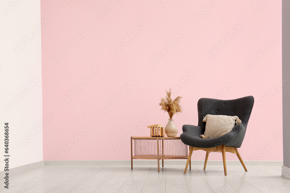 Grey armchair and vase with pampas grass on coffee table near pink wall