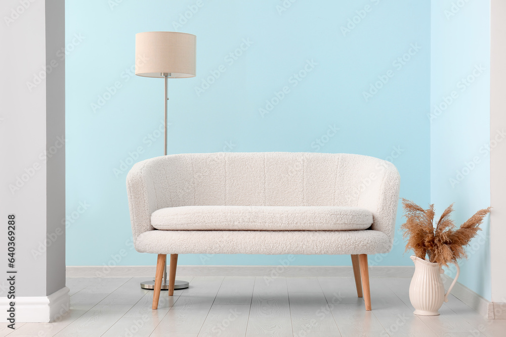 White sofa, vase with pampas grass and standard lamp near blue wall