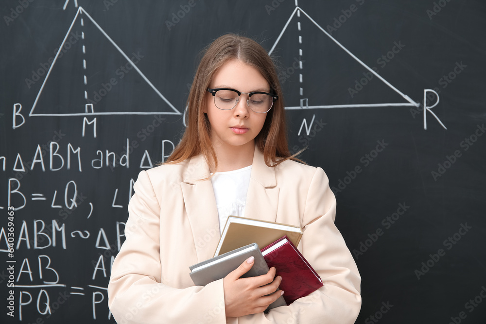 Young math teacher with books near blackboard in classroom