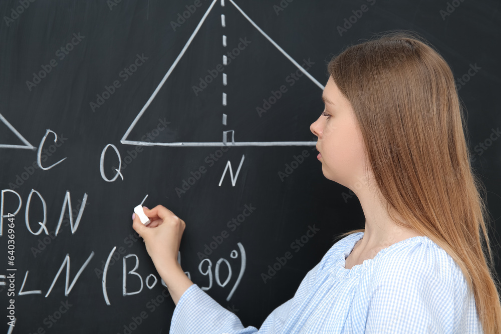 Young math teacher writing on blackboard in classroom