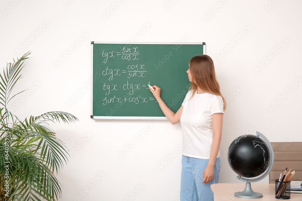 Young math teacher writing on blackboard in classroom