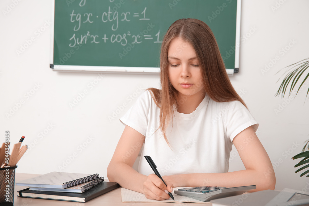 Young math teacher checking pupils homework at wooden table in classroom