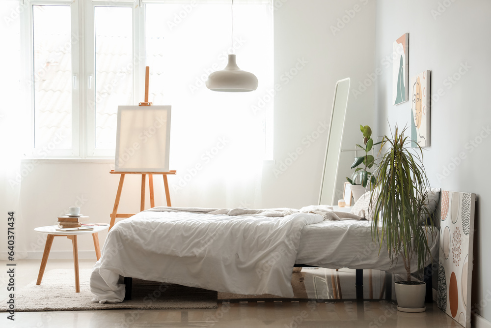 Interior of light childrens bedroom with easel and cozy bed