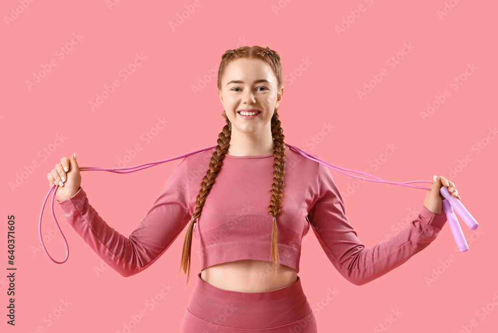 Sporty young woman with skipping rope on pink background