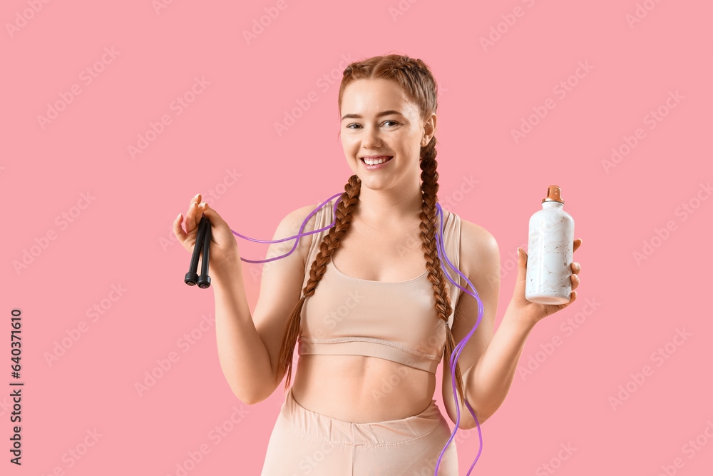 Sporty young woman with skipping rope and bottle of water on pink background