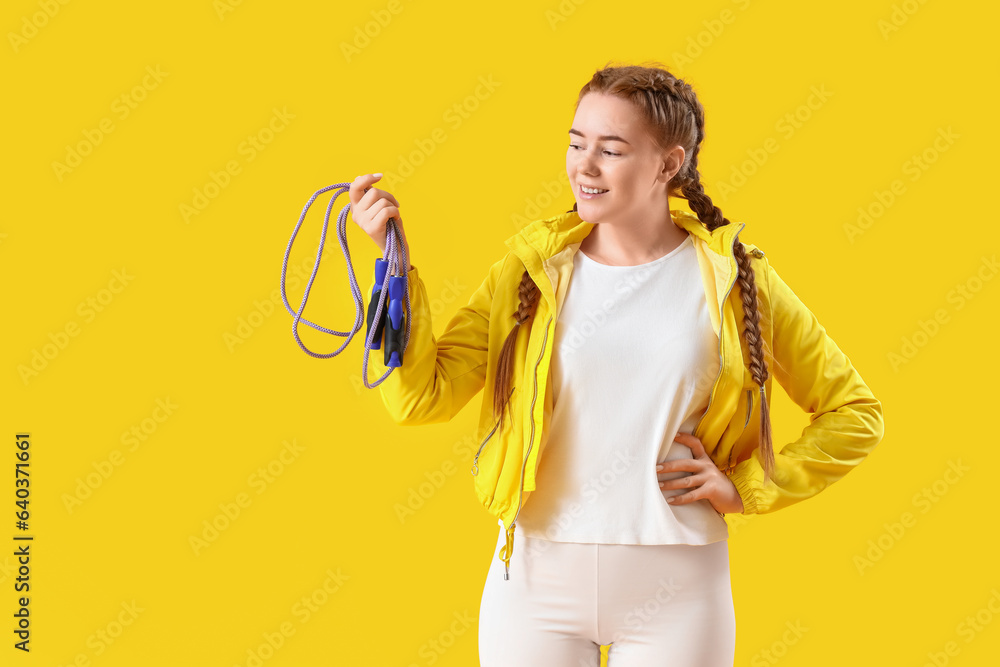 Sporty young woman with skipping rope on yellow background