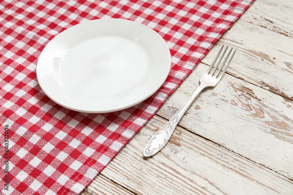 Clean plate, fork and napkin on light wooden background