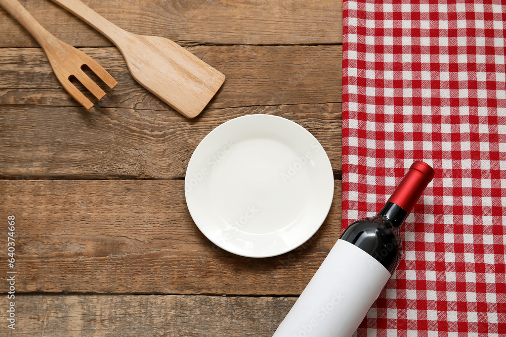 Clean plate, bottle of wine, fork and spatula on wooden background