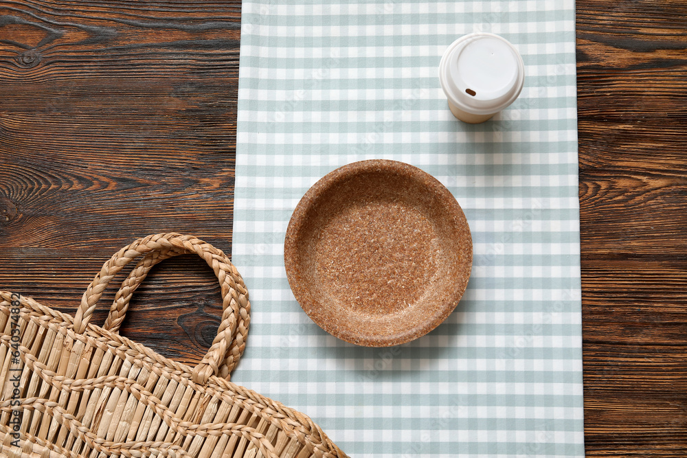 Disposable plate, cup, wicker bag and napkin on wooden background