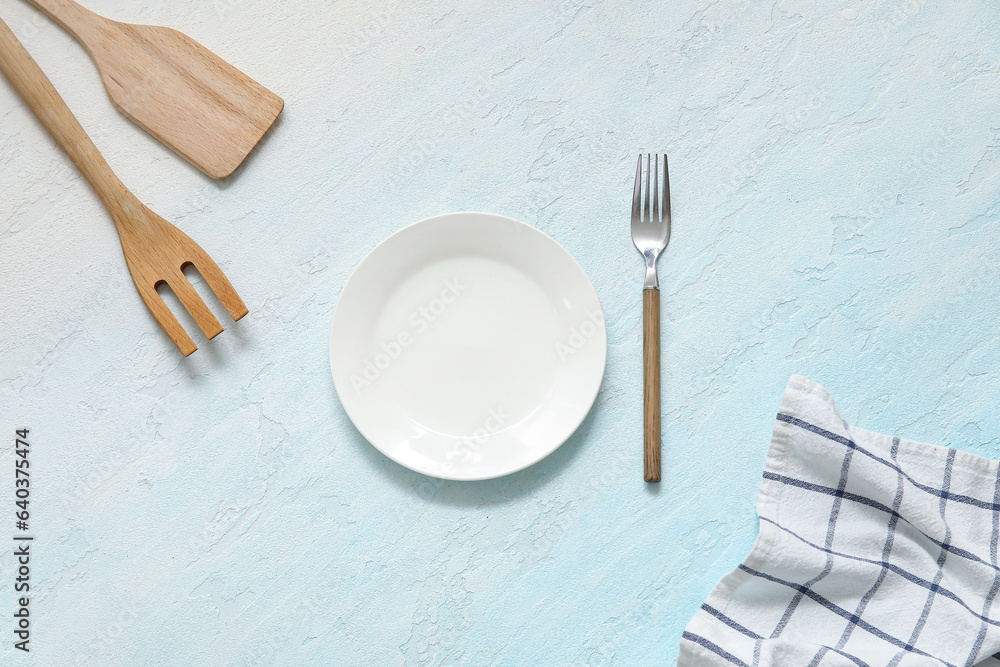 Clean plate, spatula, forks and napkin on blue background