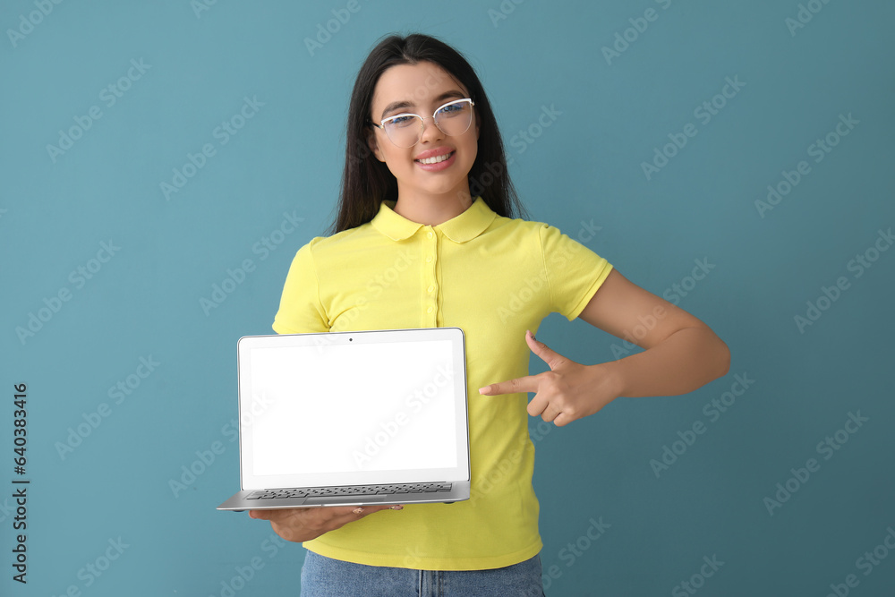 Happy young female programmer pointing at laptop on blue background