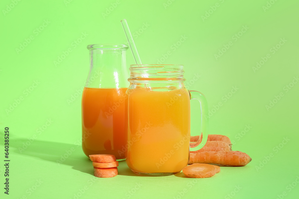 Mason jar and bottle of fresh carrot juice on green background