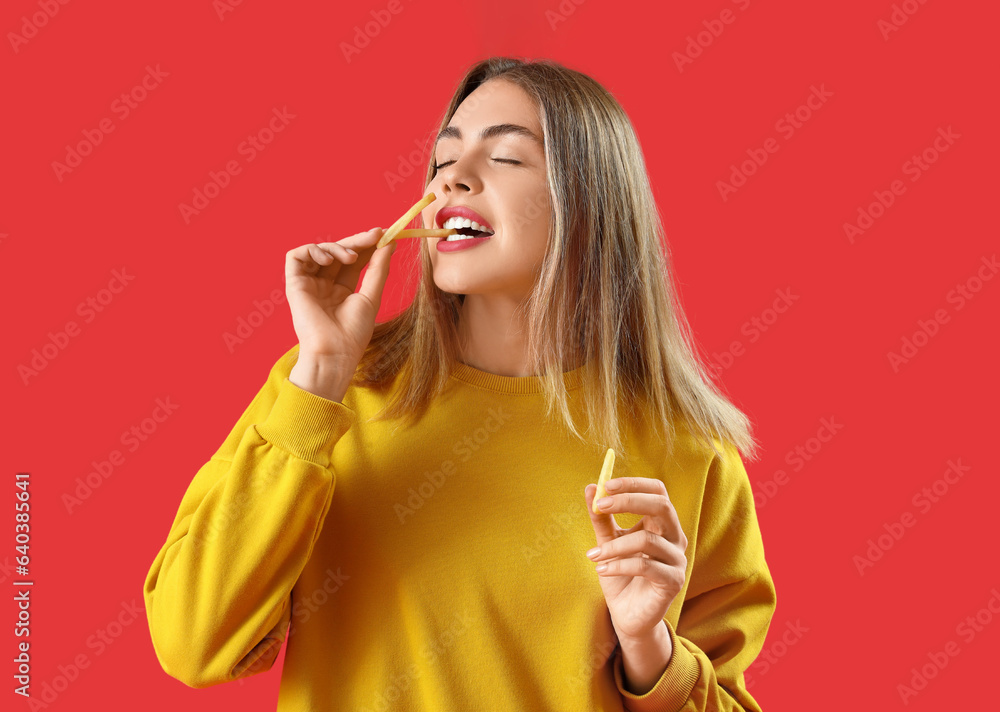 Beautiful young woman eating french fries on red background