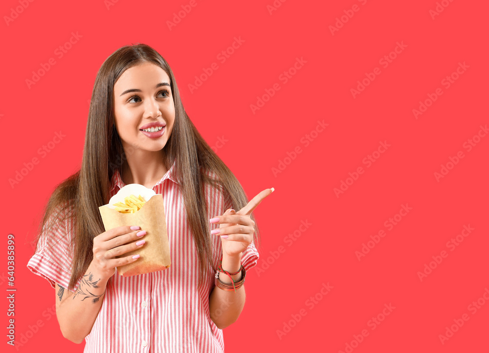 Beautiful thoughtful young woman with french fries pointing at something on red background