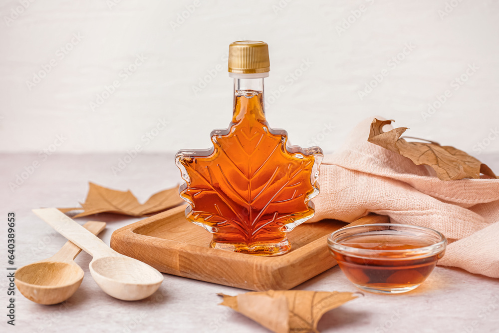 Bottle and bowl of tasty maple syrup on light background