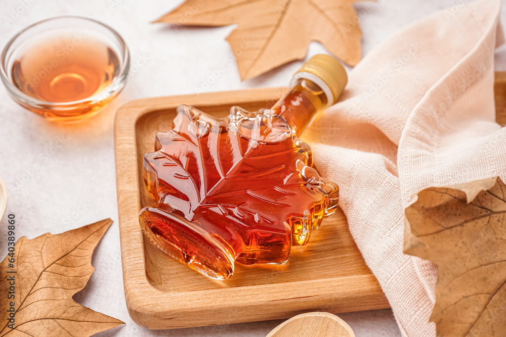 Bottle of tasty maple syrup on light background