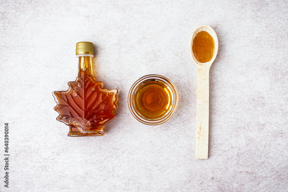 Bottle, bowl and spoon of tasty maple syrup on light background