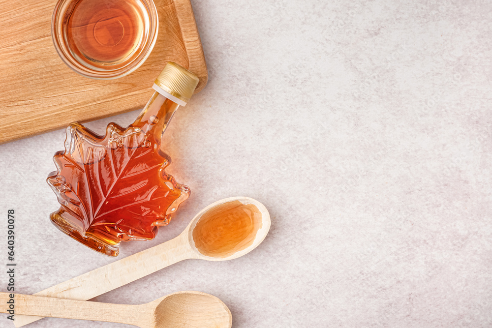 Bottle, bowl and spoons of tasty maple syrup on light background