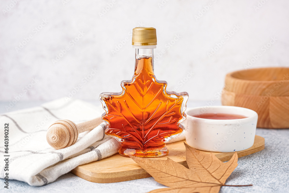 Bottle and bowl of tasty maple syrup on table