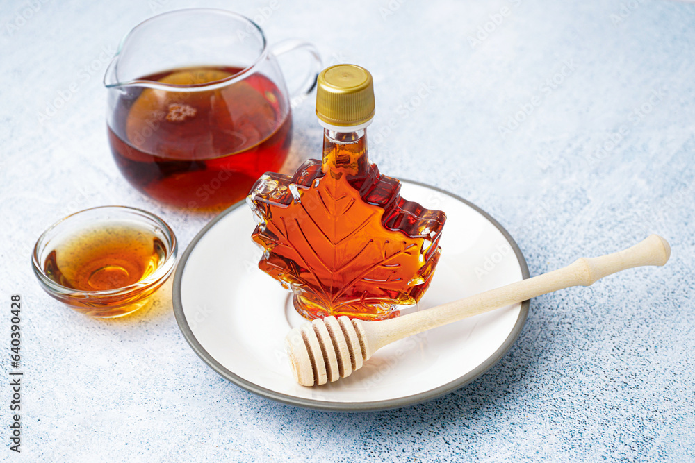 Bottle and bowl of tasty maple syrup on grey background