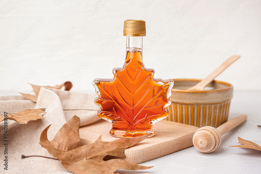 Bottle of tasty maple syrup on light background