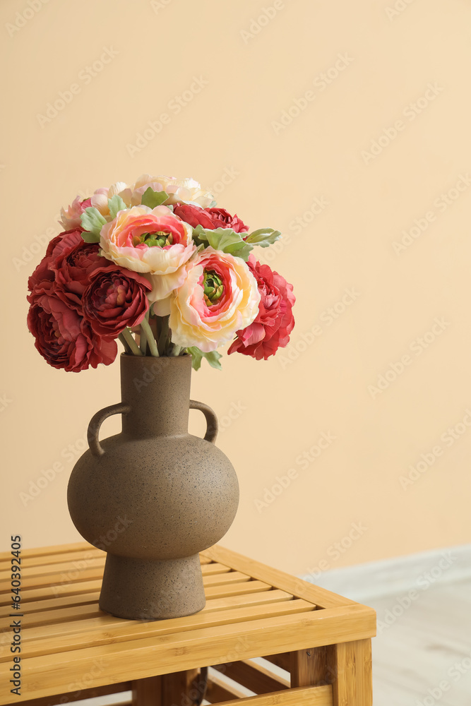 Vase with beautiful peony flowers on wooden table near beige wall, closeup