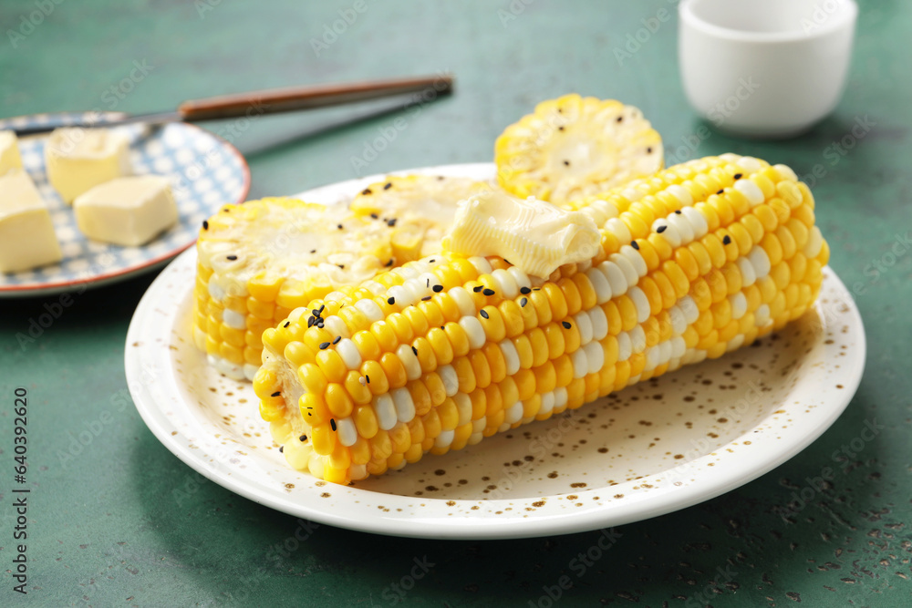 Plate of boiled corn cobs with butter on green background