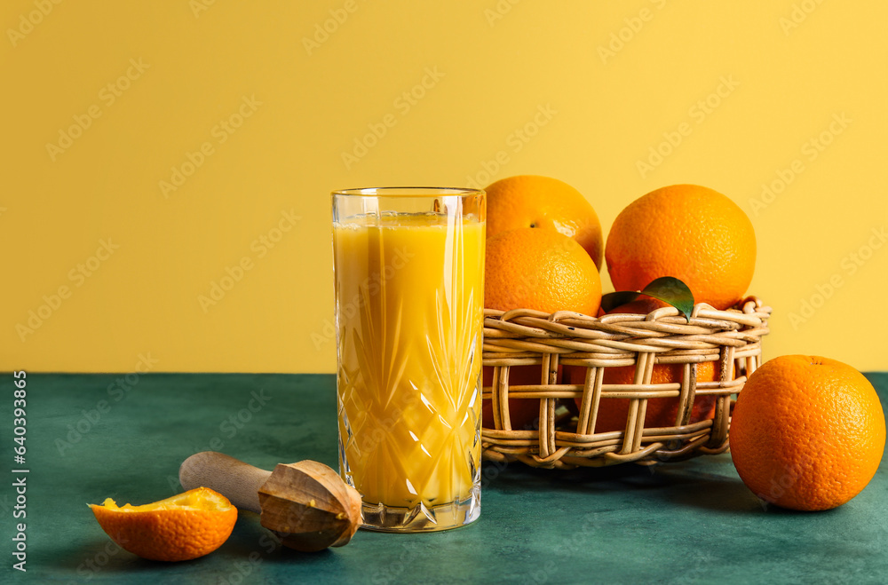 Glass of fresh orange juice and wooden juicer on green table