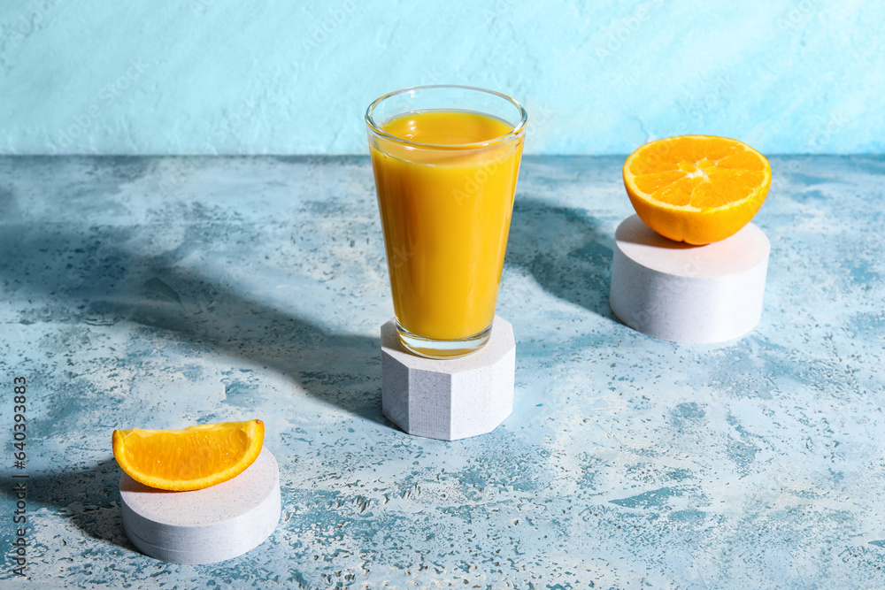 Decorative podium with glass of fresh orange juice on blue background