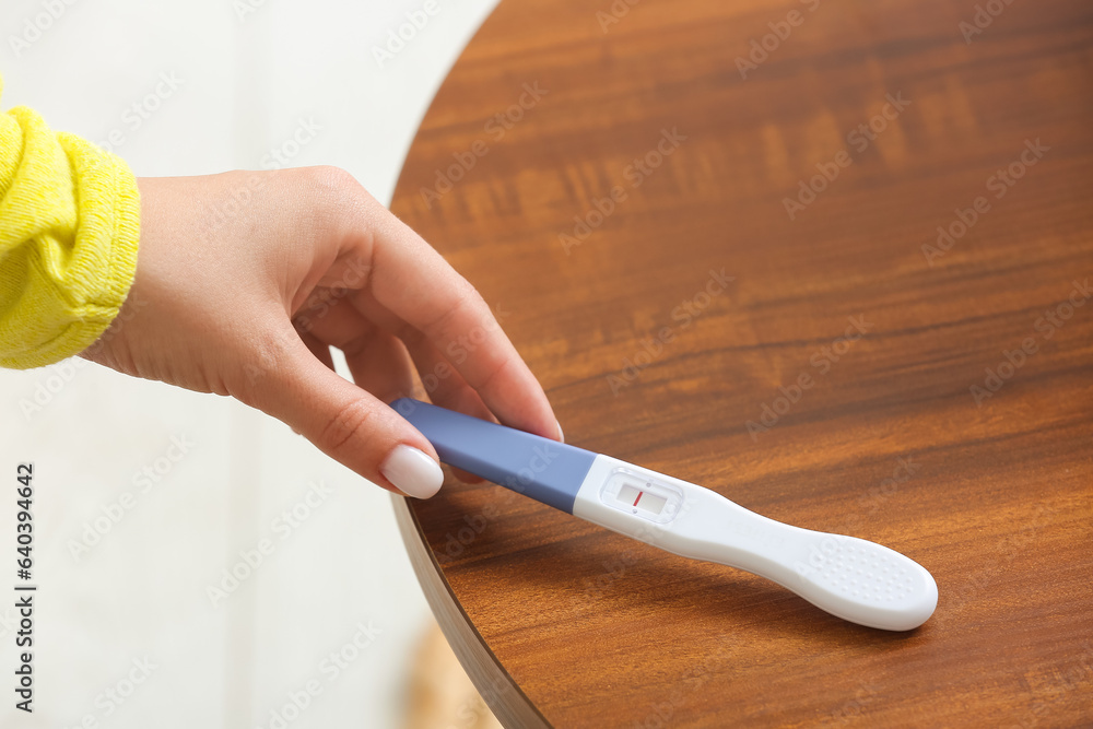 Female hand with negative pregnancy test on wooden table, closeup