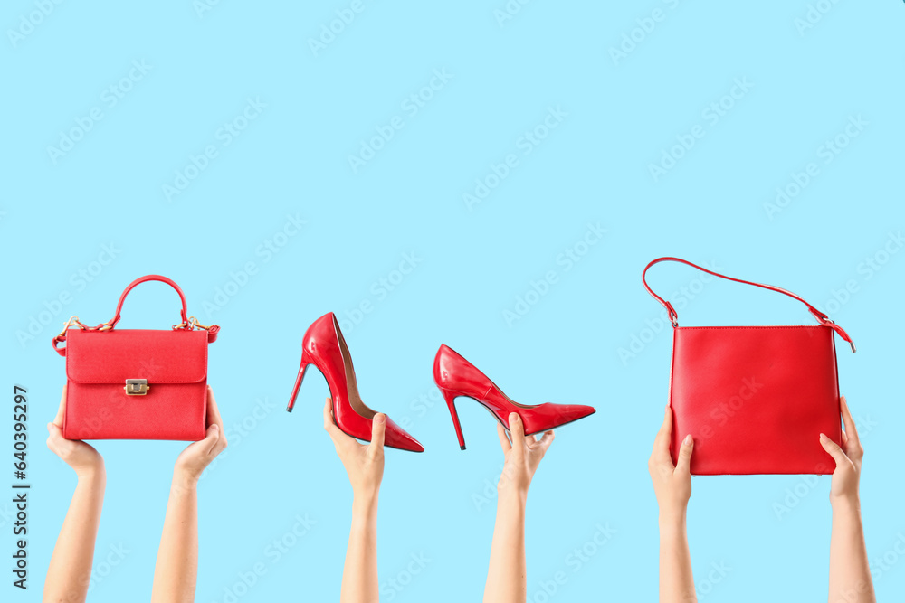 Female hands holding stylish womens bags and shoes on blue background