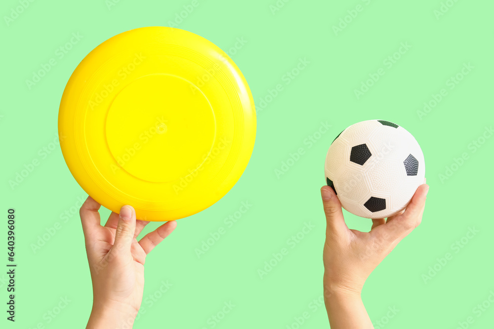 Female hands holding flying disc and soccer ball on green background