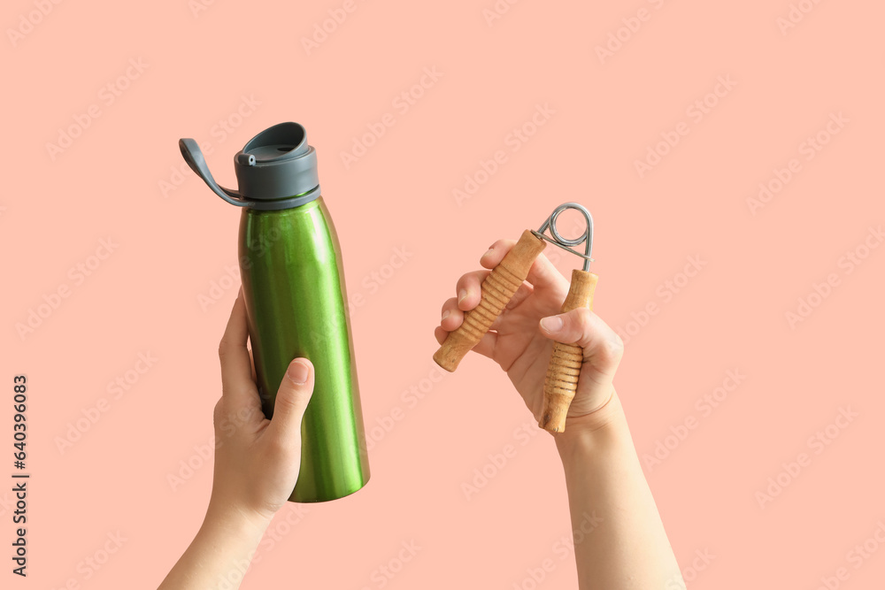 Female hands with sport bottle of water and expander on pink background