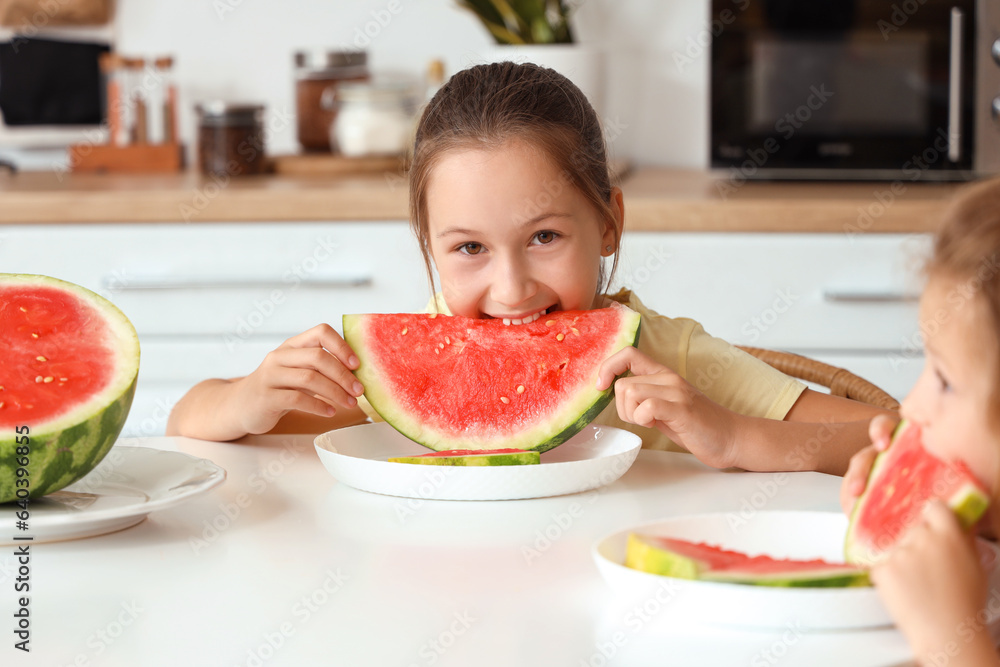 Happy little girls with slices of fresh watermelon sitting at table in kitchen