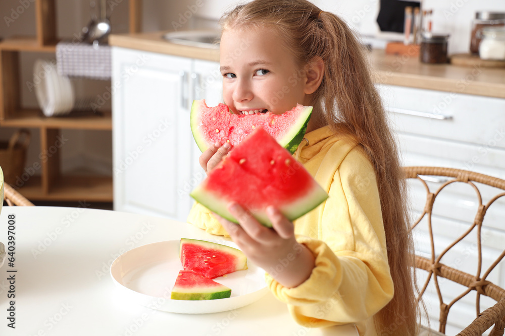 Happy little girl eating fresh watermelon and sitting at table in kitchen