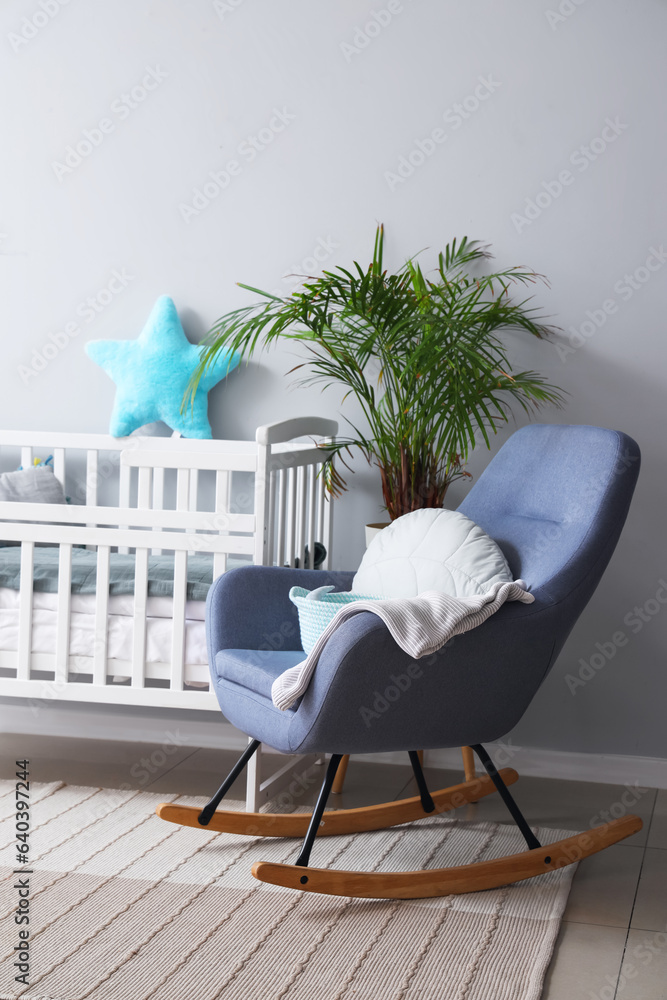 Interior of childrens room with crib and rocking chair near white wall