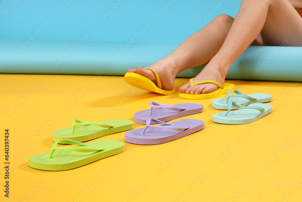 Female legs with different colorful flip flops on color background